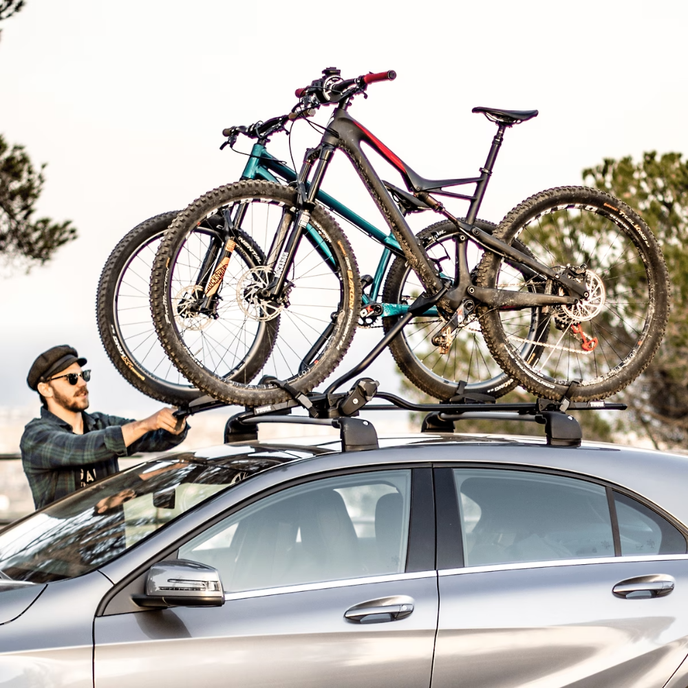 Man loading bicycles onto a car roof rack with a scenic background
